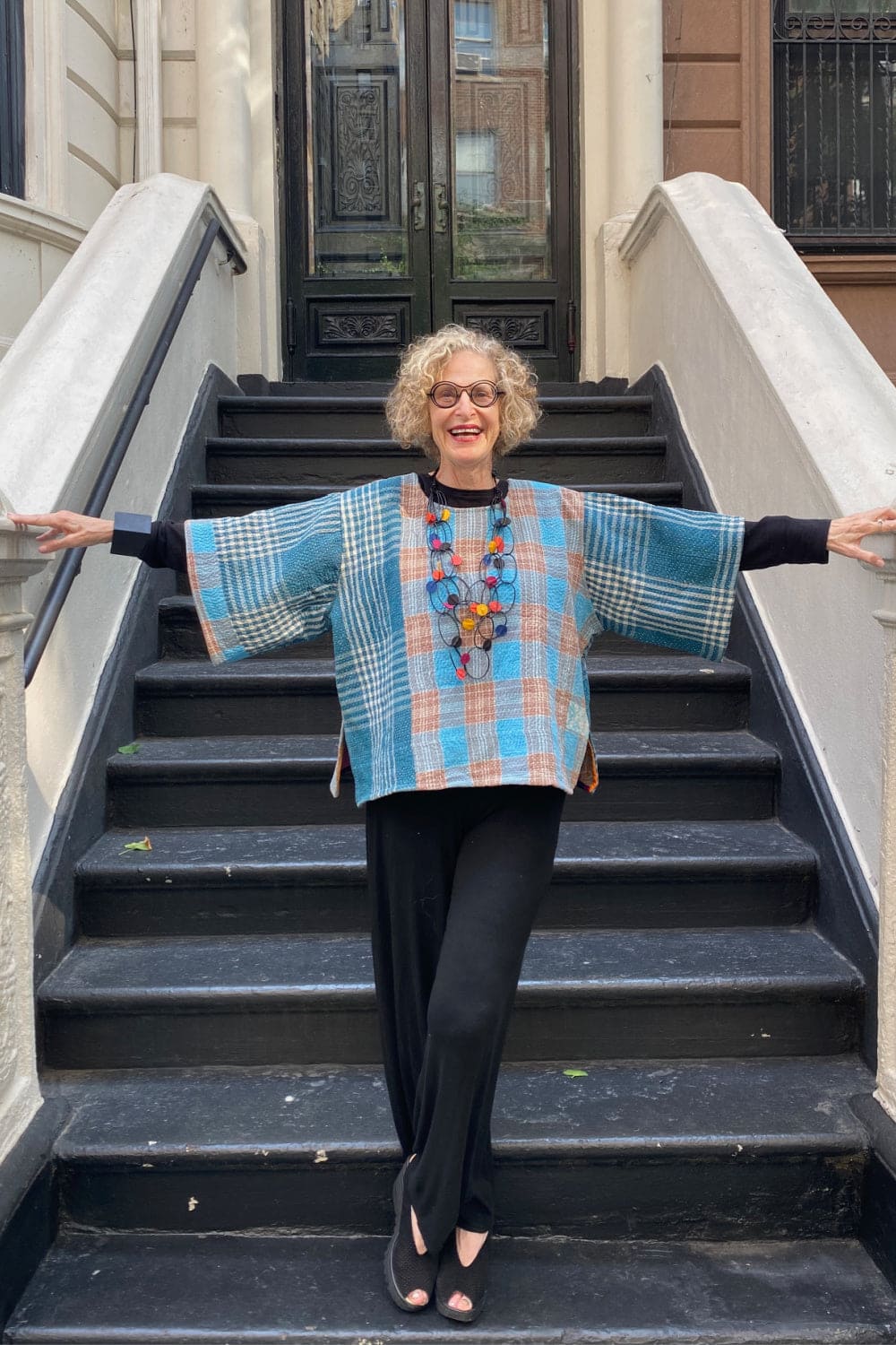 Older woman wearing a boxy plaid pullover with a statement necklace.