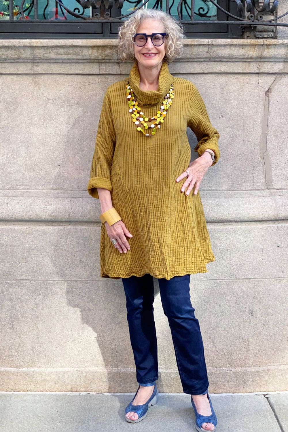 Stylish older woman wearing a mustard color cowl tunic with jeans.