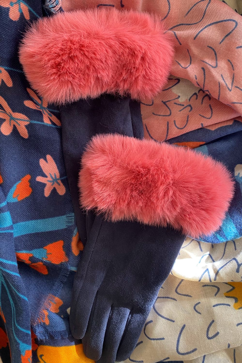 Pink and navy faux fur trim gloves laying ontop of matching color scarf.