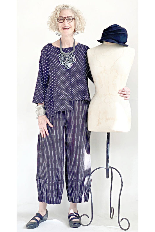 Black merino wool brim woman's hat resting on a mannequin. Older woman wearing a coordinating stylish outfit is standing beside.