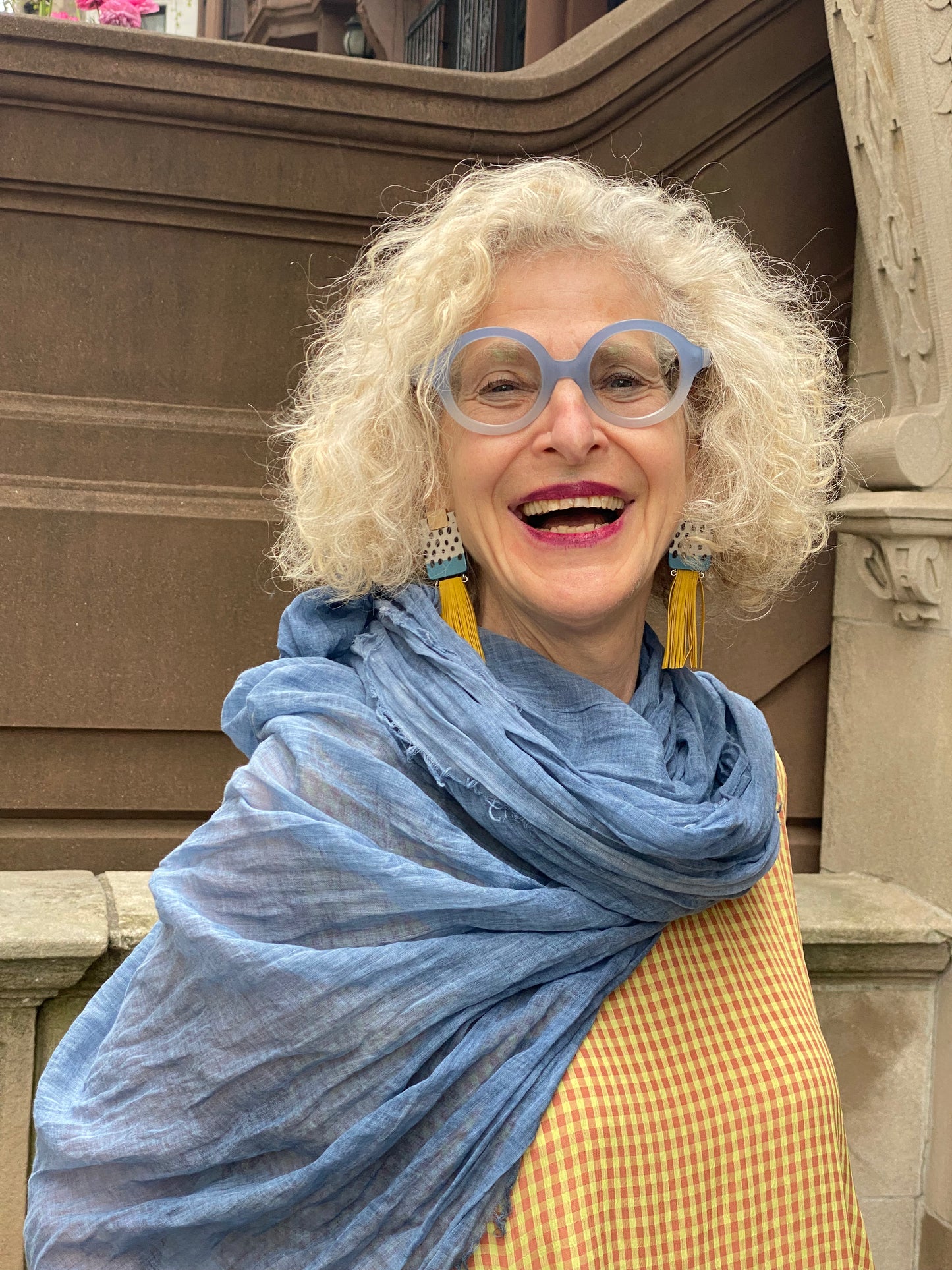 Smiling woman wearing pretty yellow tassel earrings, blue cotton scarf and baby check yellow/rose dress.