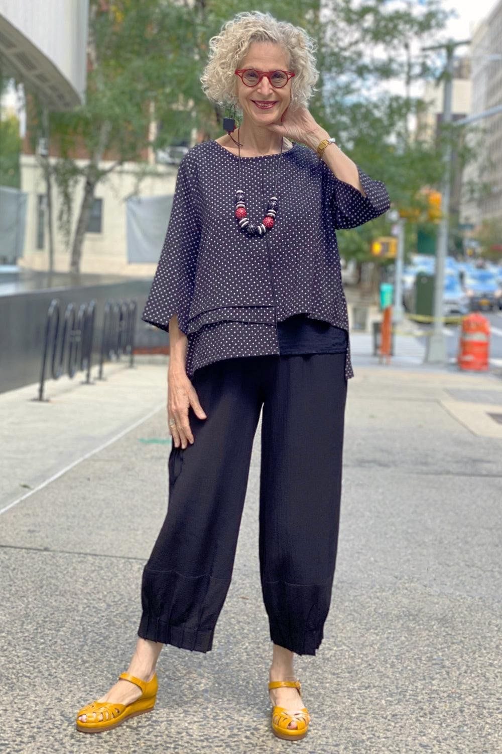 Smiling woman on the street wearing a black and white polka dot top with black and red earrings and necklace. She has blond hair and is a woman of a certain age.