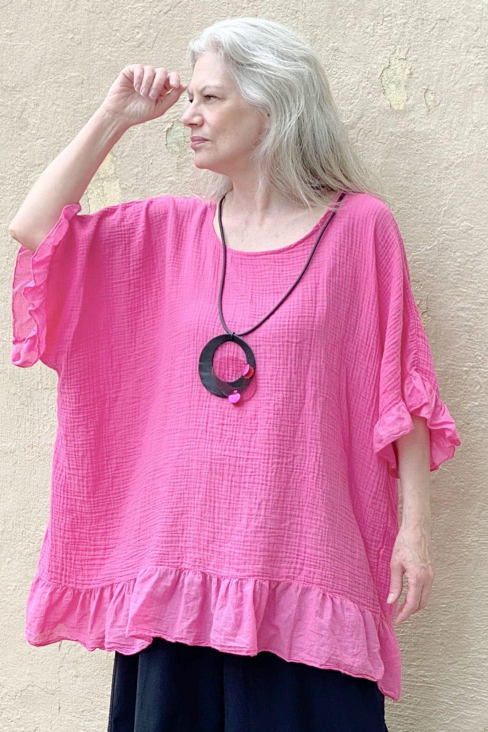 Woman wearing a pink ruffled tunic with black full cut pants and a black & pink pendant