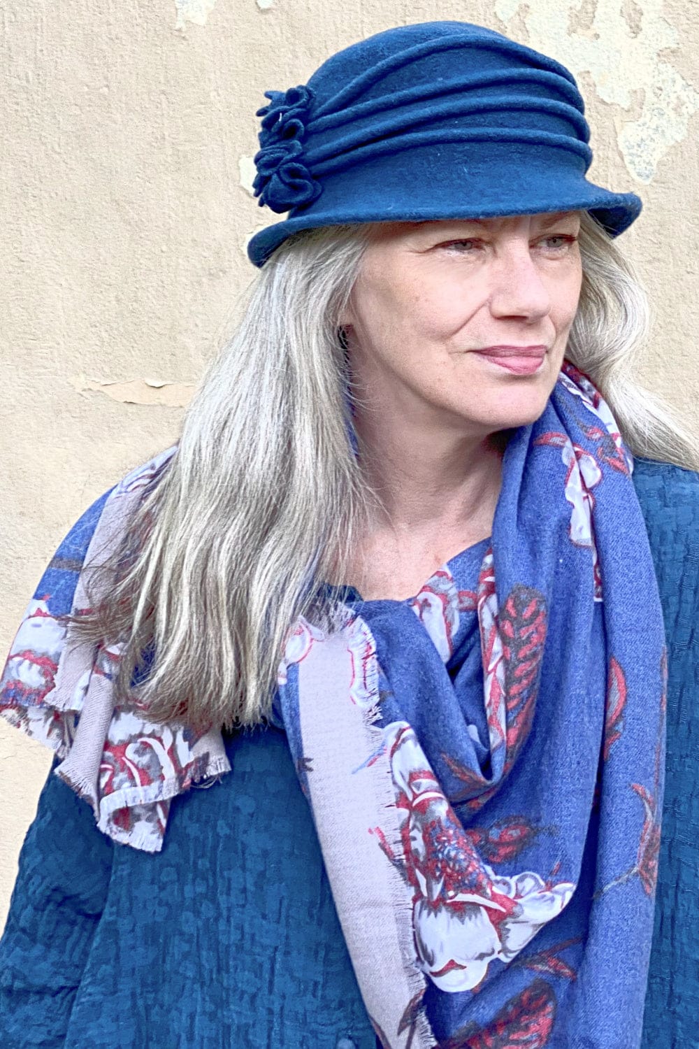 Grey haired woman wearing a blue wool hat styled with a floral blue scarf.