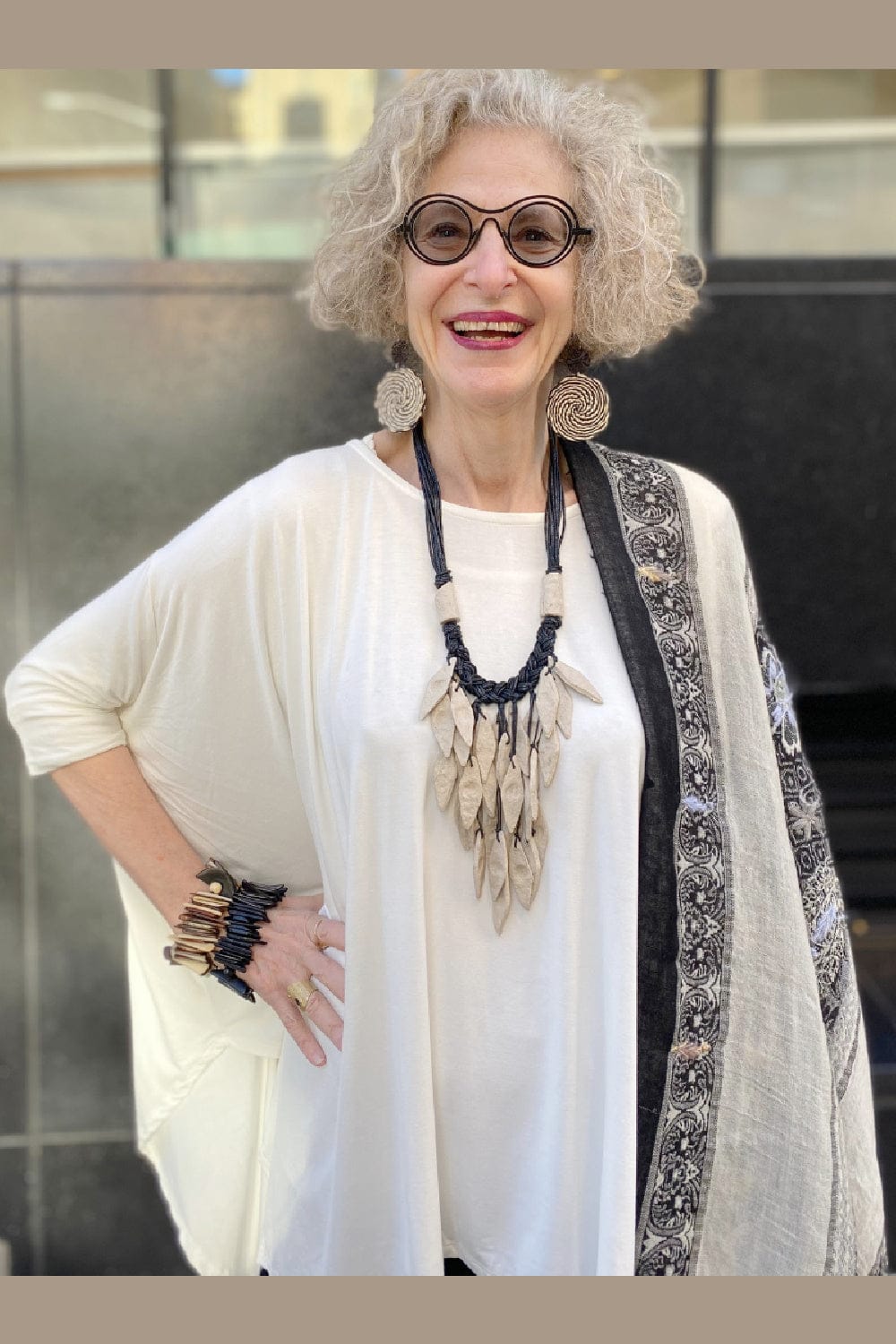 Smiling woman with curly blong hair modeling a oversize white top with accessories.