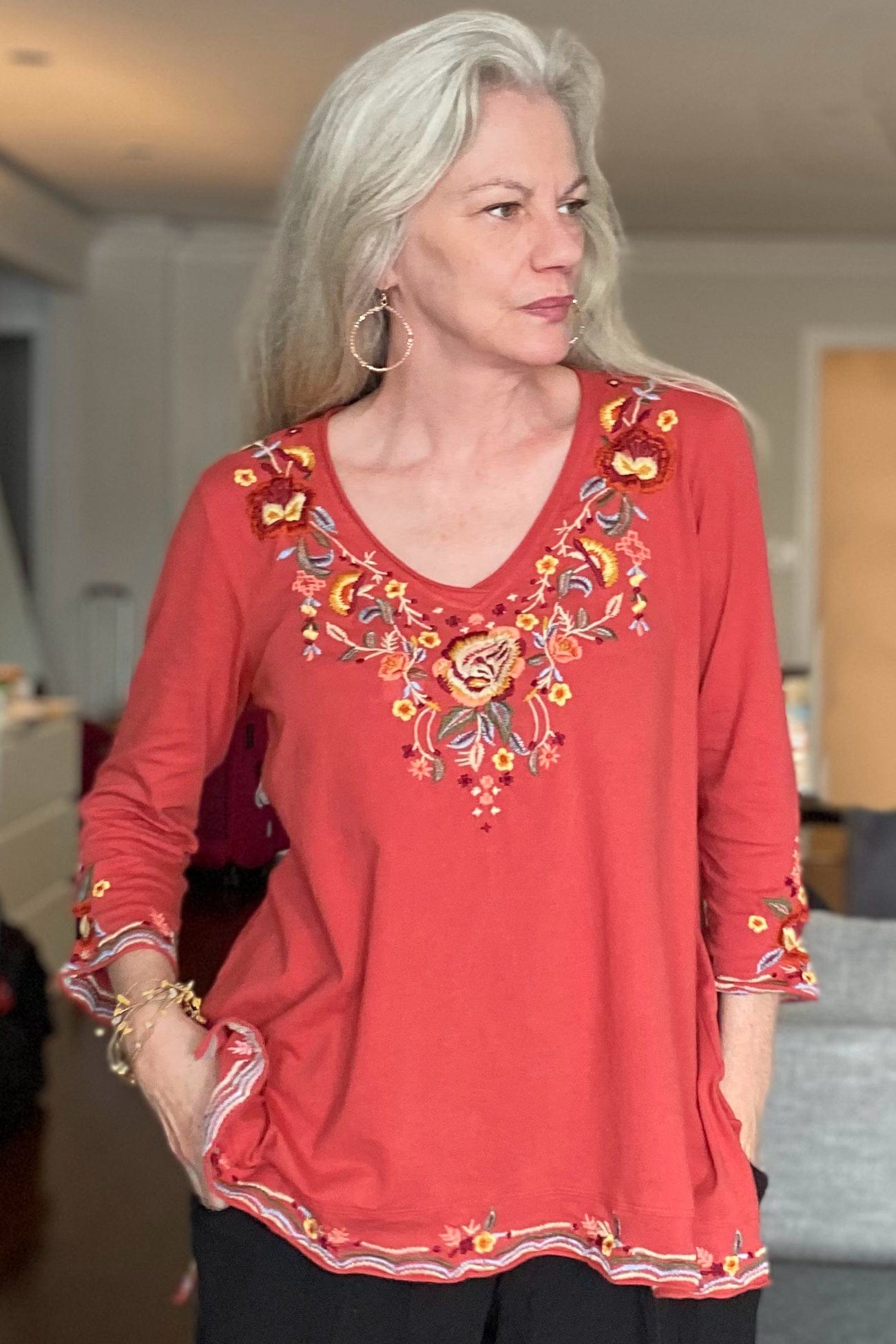 Glass bead hoop earrings worn on a grey hair woman styled with an embellished v neck top and wire bracelet.